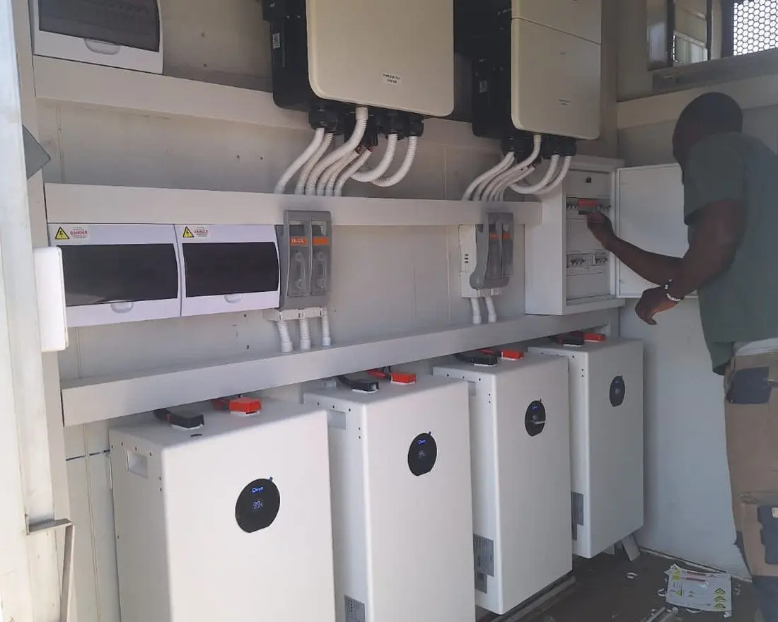 Technician working at a wall of inverters above a bank of battery units