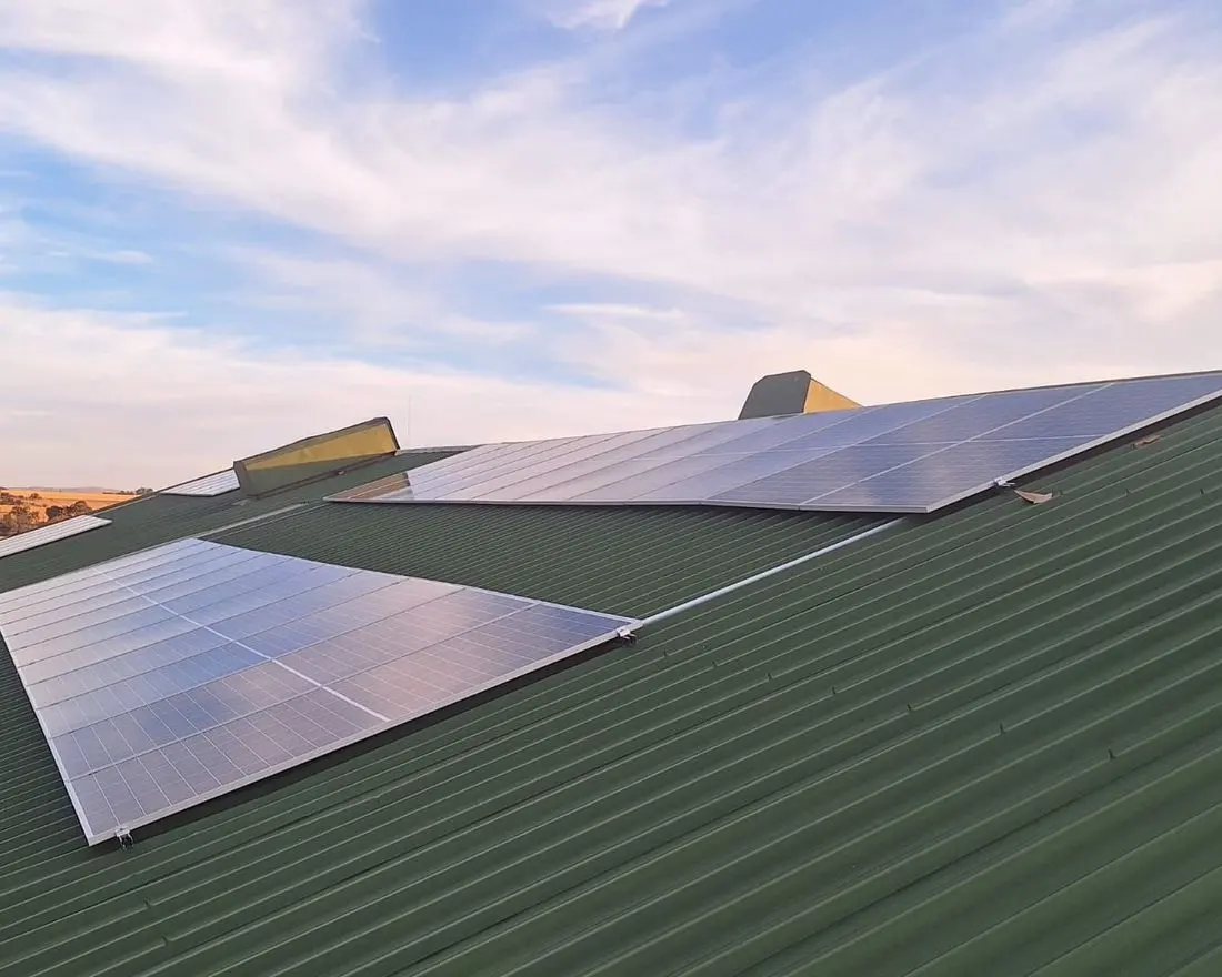 Solar panels mounted across a pitched metal roof against an evening sky