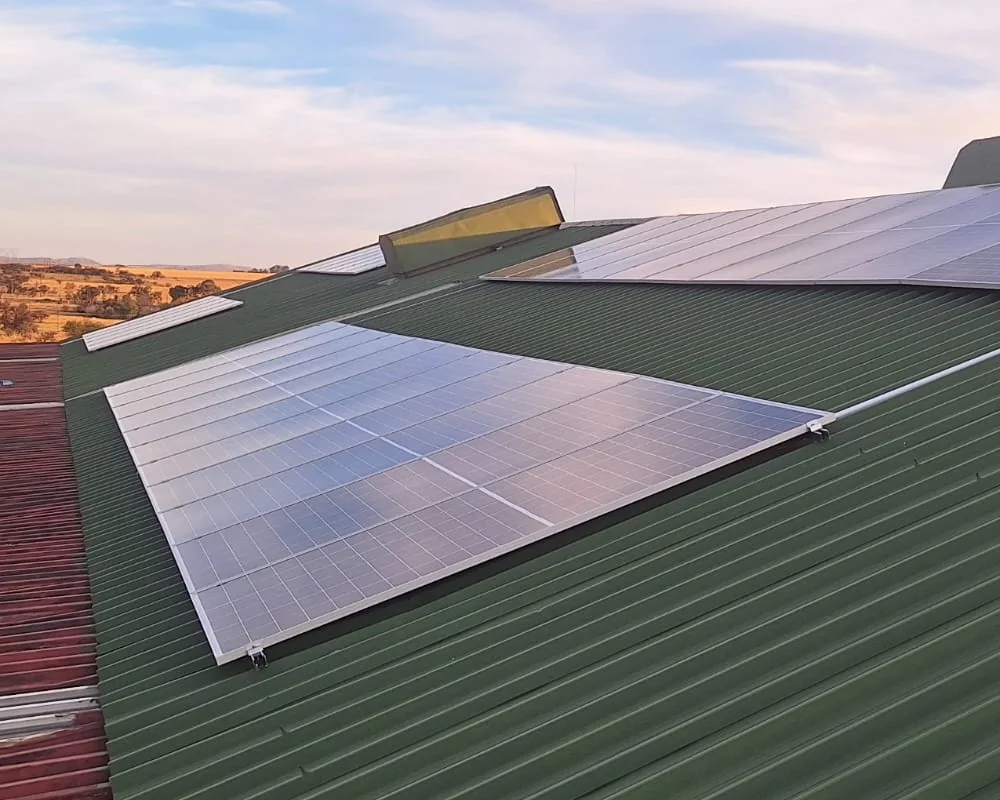 Roof-mounted solar array on a green corrugated roof, with open veld beyond